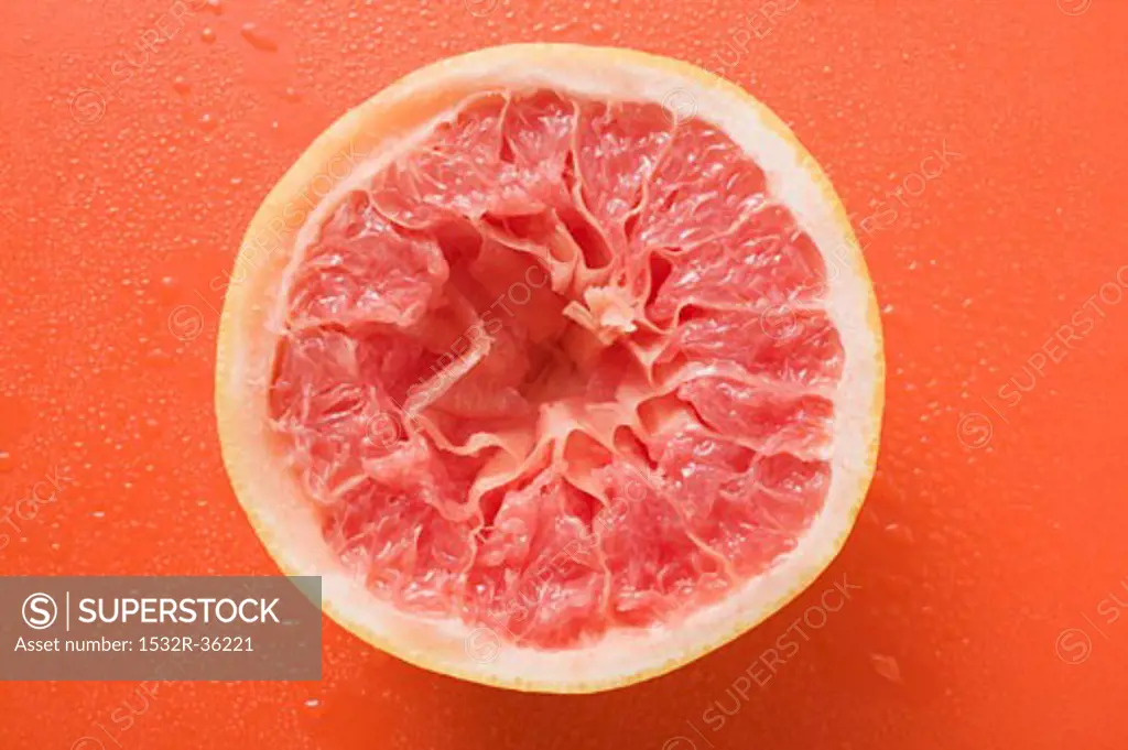 Squeezed pink grapefruit on orange background