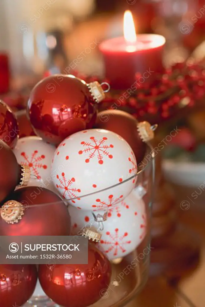 Assorted Christmas tree baubles in front of red candle