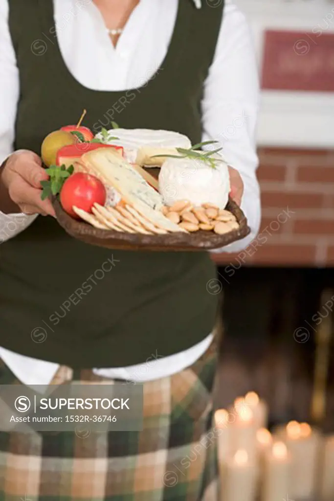 Woman holding cheeseboard with fruit & crackers (Christmas)