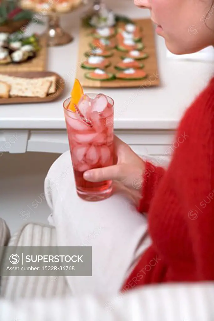 Woman holding glass of Campari with ice cubes, snacks in background