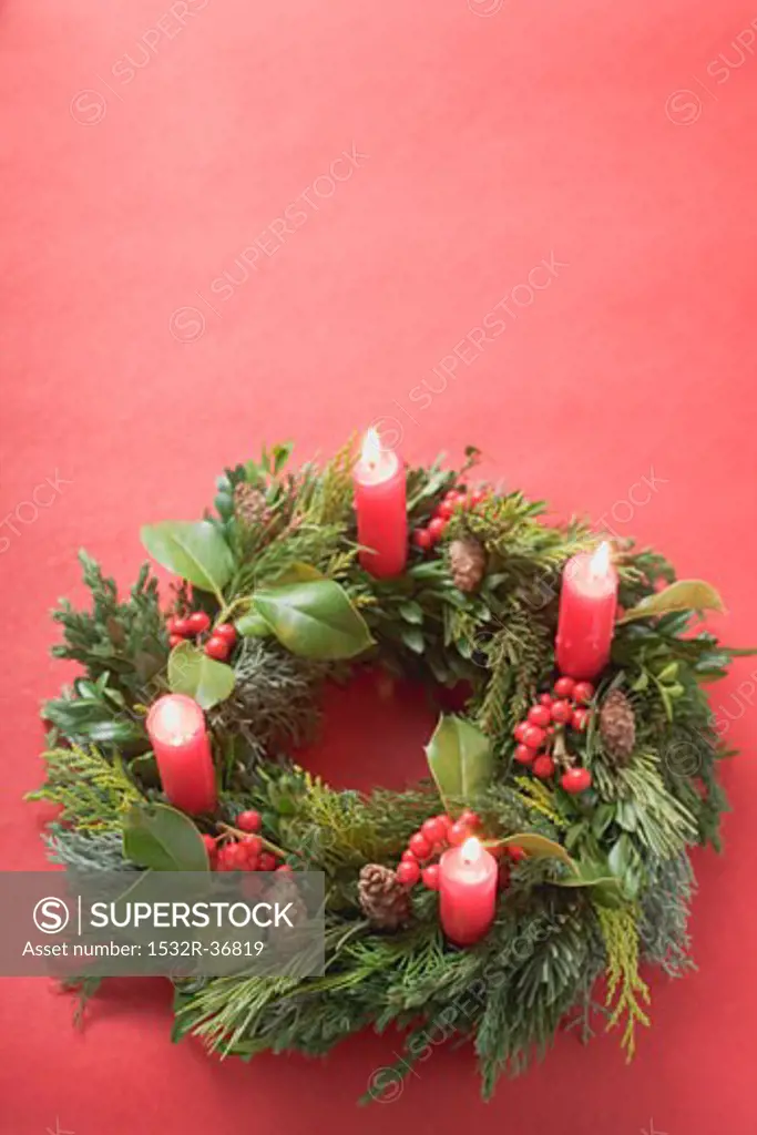 Advent wreath with four burning candles on red background