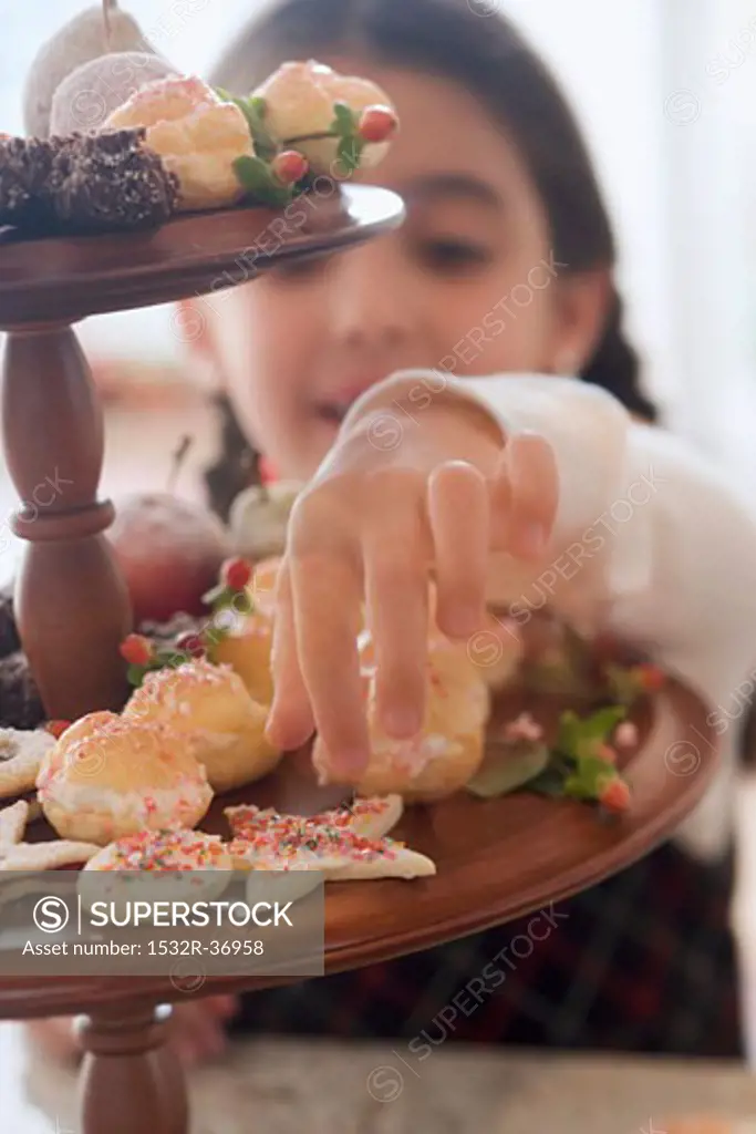 Girl reaching for Christmas biscuit on tiered stand