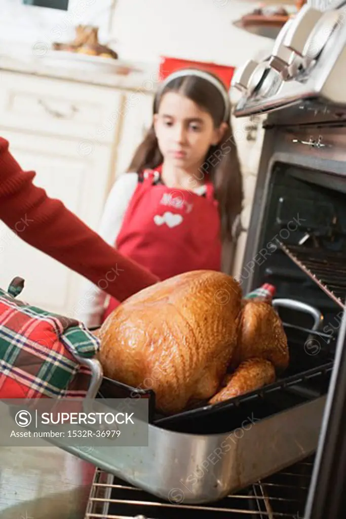 Woman taking turkey out of oven, girl in background