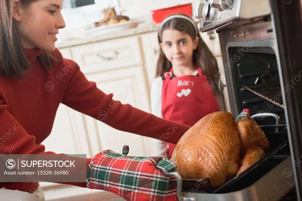 Woman taking turkey out of oven, girl in background