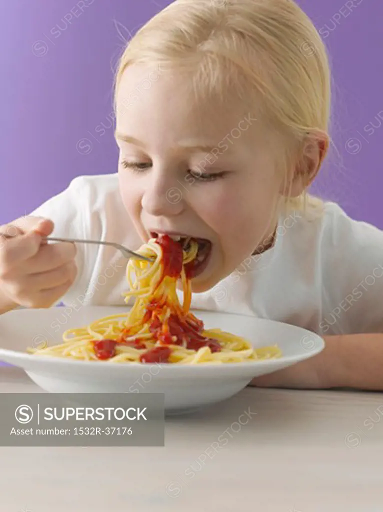 Blond girl eating spaghetti with tomato sauce