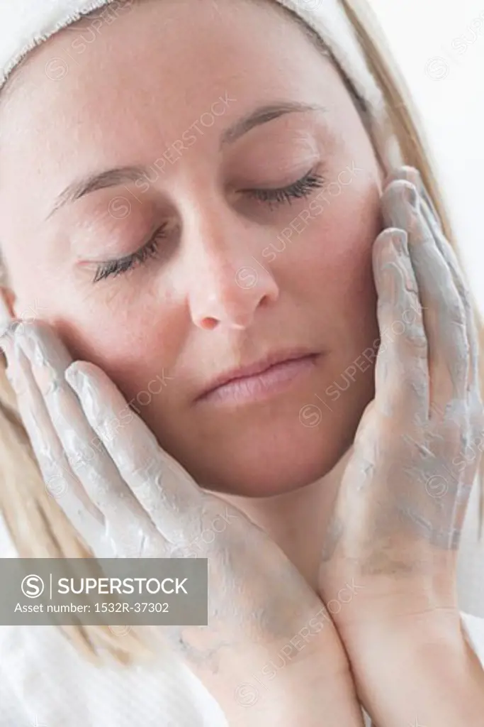 Young woman putting cream on her face