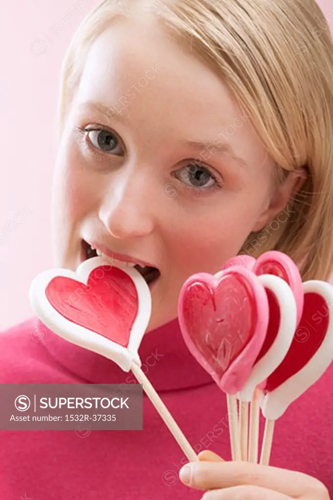 Young woman biting into a heart-shaped lollipop