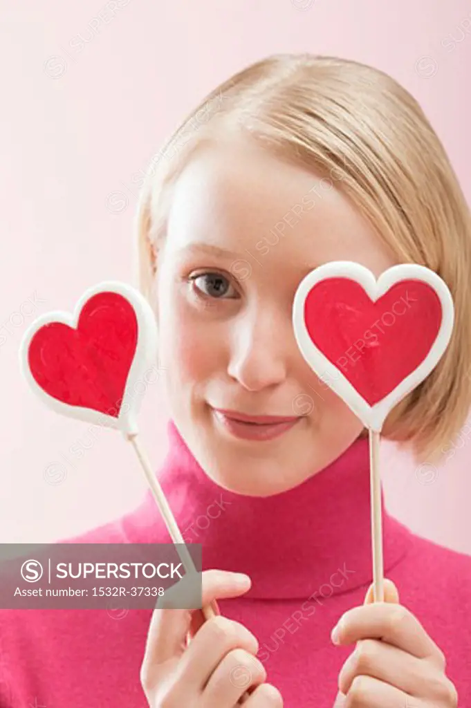 Young woman with heart-shaped lollipops in front of her eyes
