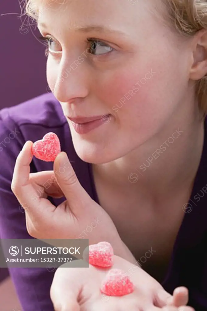 Young woman eating sugar-coated, heart-shaped jelly sweets