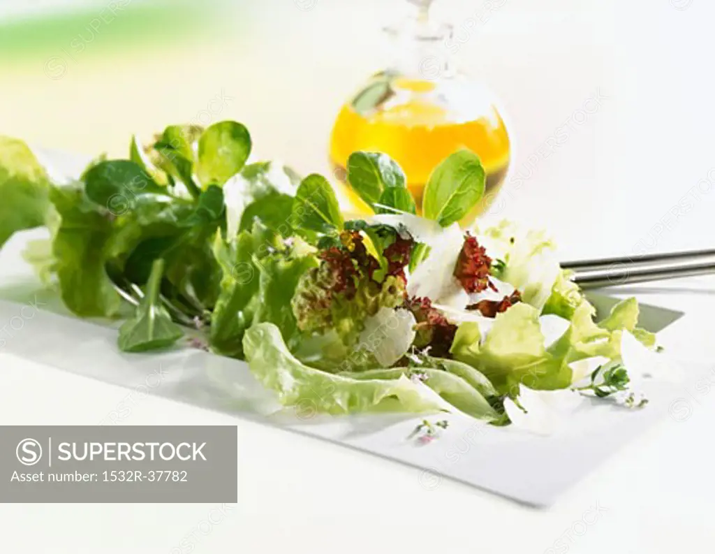 Mixed salad with Parmesan, bottle of oil in background