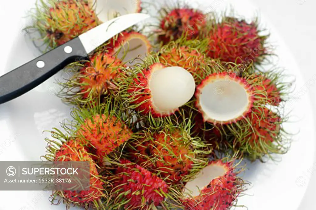 Whole and peeled rambutans on a plate with knife