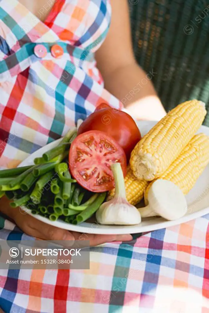 Woman holding plate of vegetables & corn on the cob for grilling