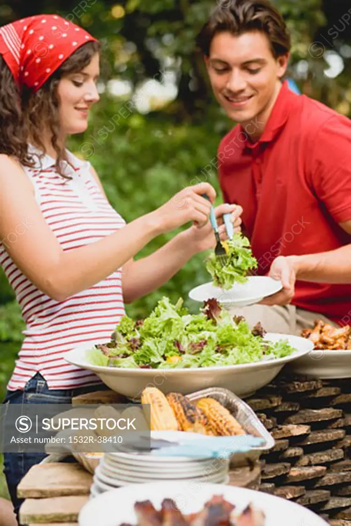 Young woman serving green salad at a barbecue
