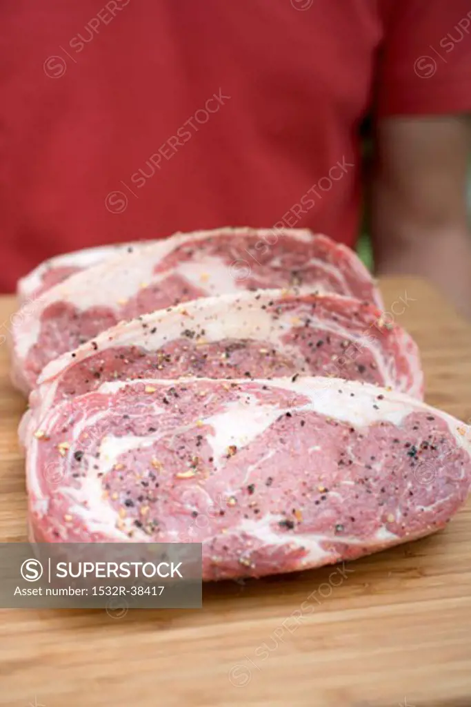 Seasoned steaks on chopping board, man in background