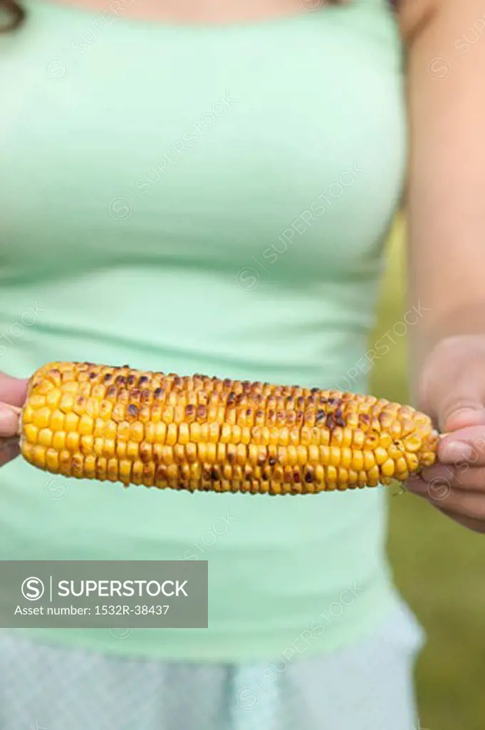 Woman holding grilled corn on the cob