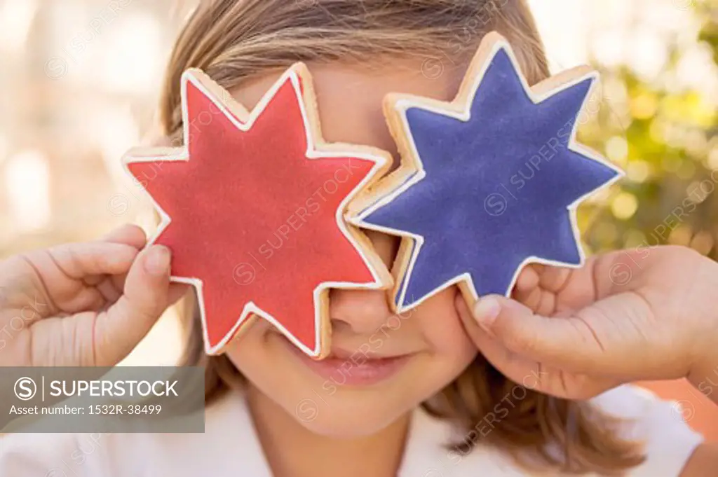 Small girl holding two star cookies in front of her eyes