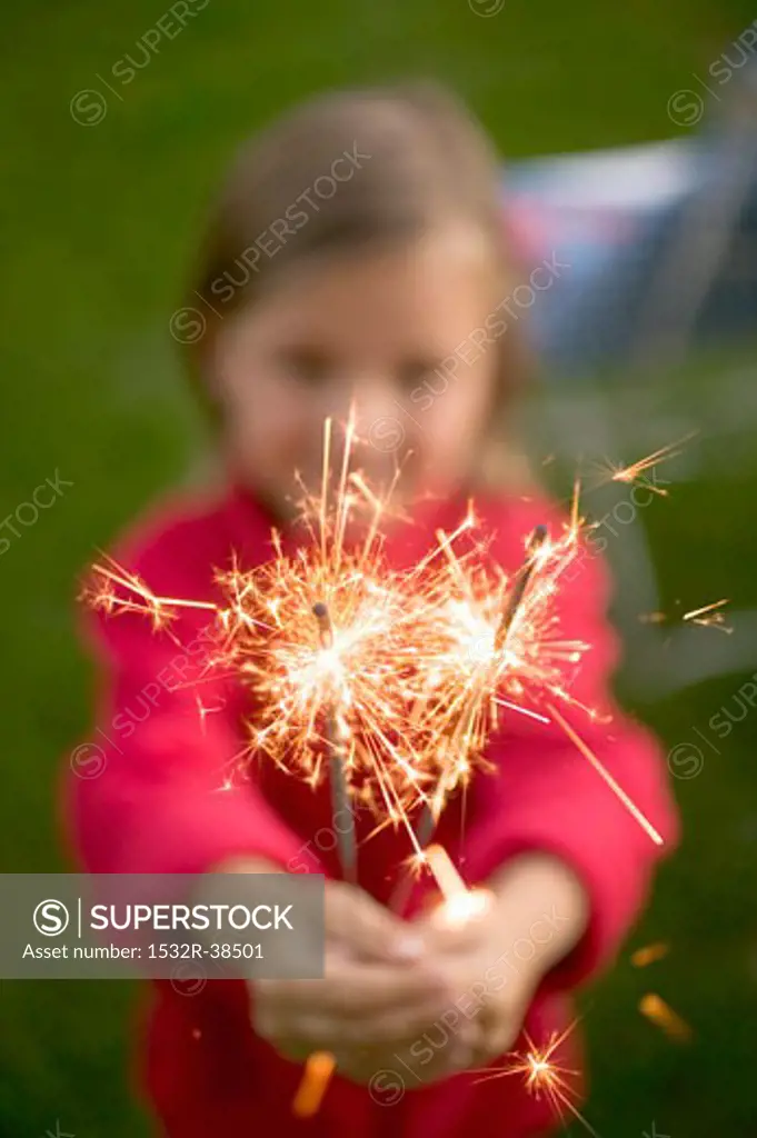 Small girl holding sparklers in garden