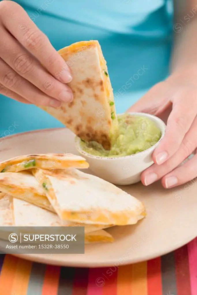 Woman dipping piece of tortilla in guacamole