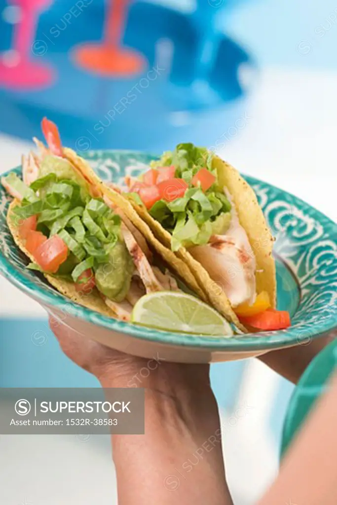 Woman holding plate of two chicken tacos