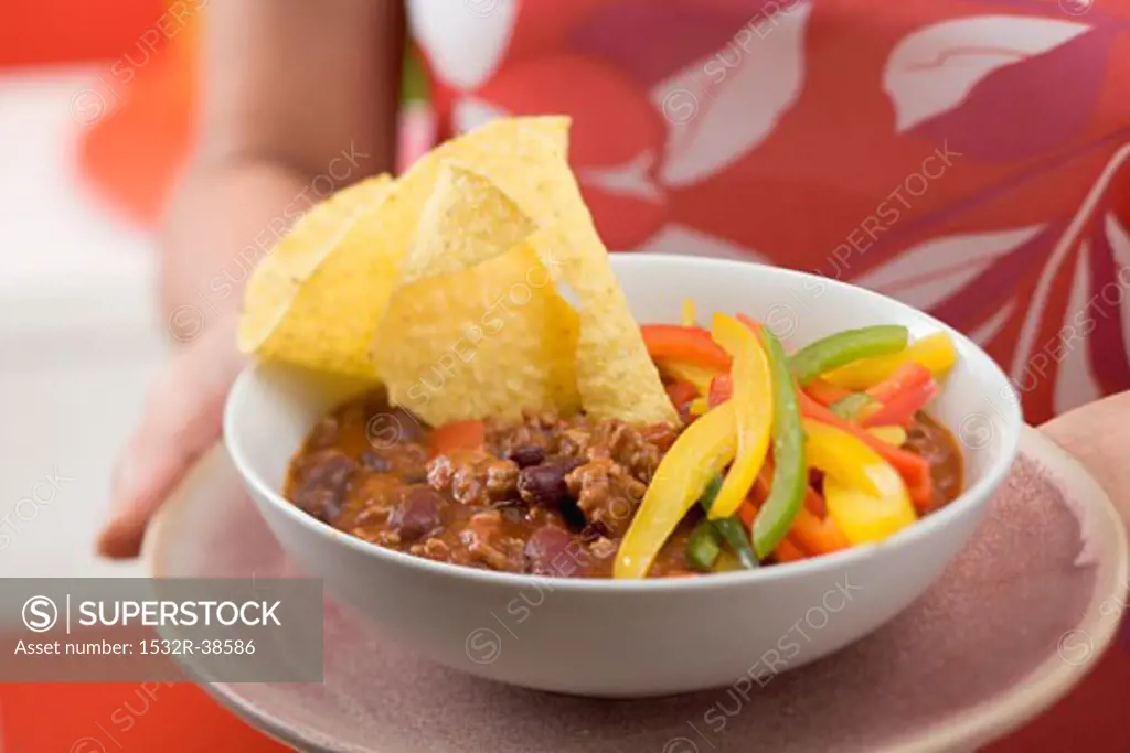 Woman serving chili con carne with nachos and peppers