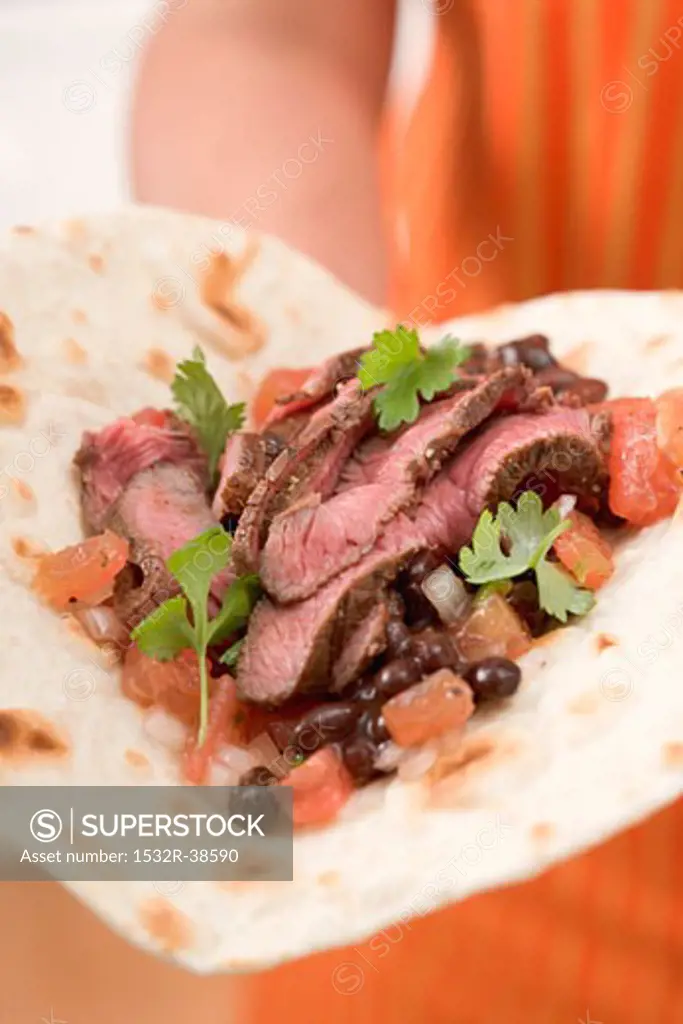 Woman holding beef fajita with beans and tomatoes