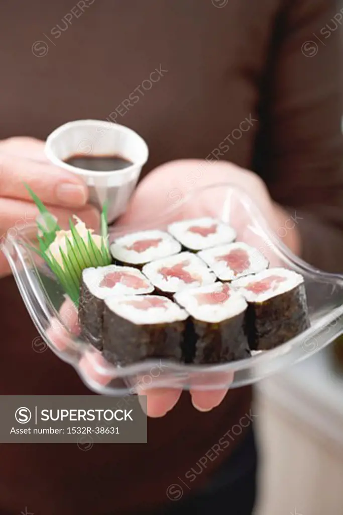Woman holding maki sushi and soy sauce on plastic tray