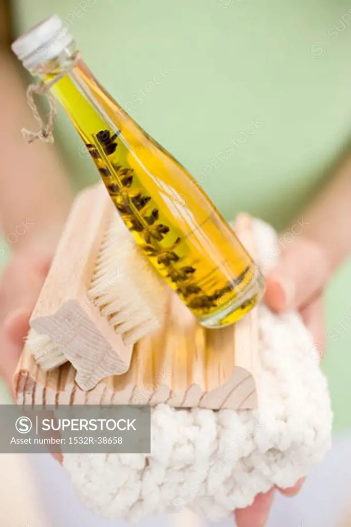 Woman holding bottle of body oil, soap dish, brush & towel