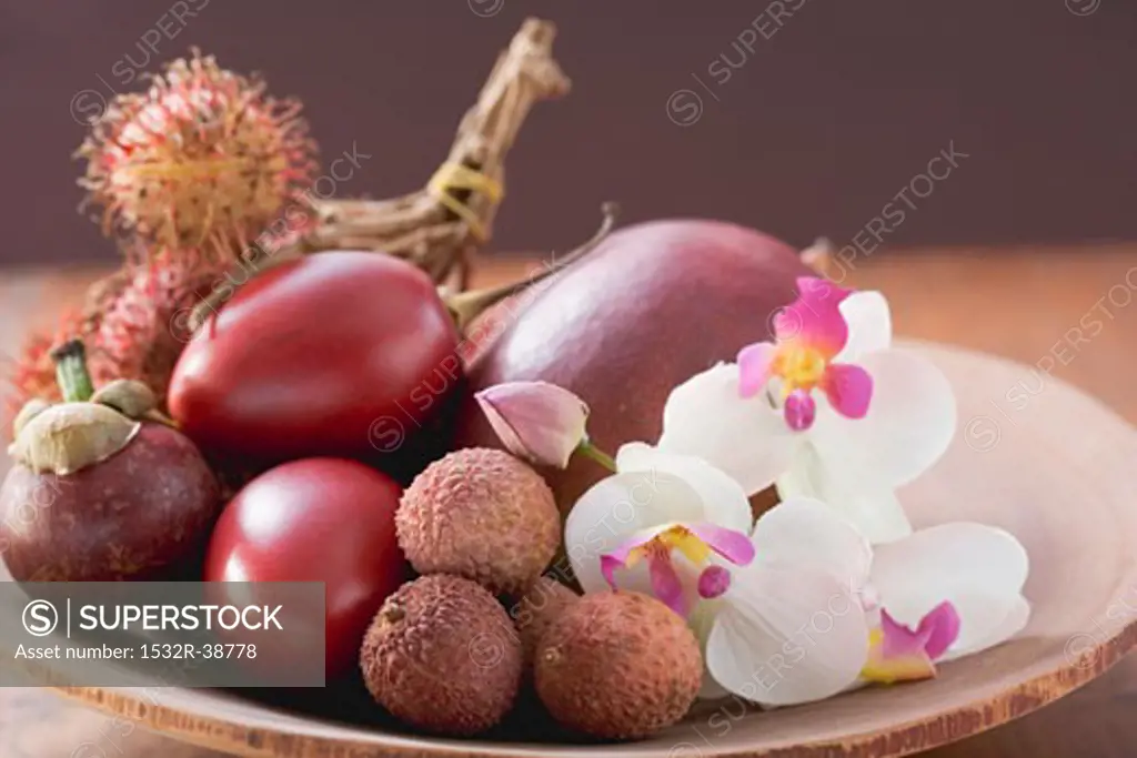 Assorted exotic fruits in a dish with orchids