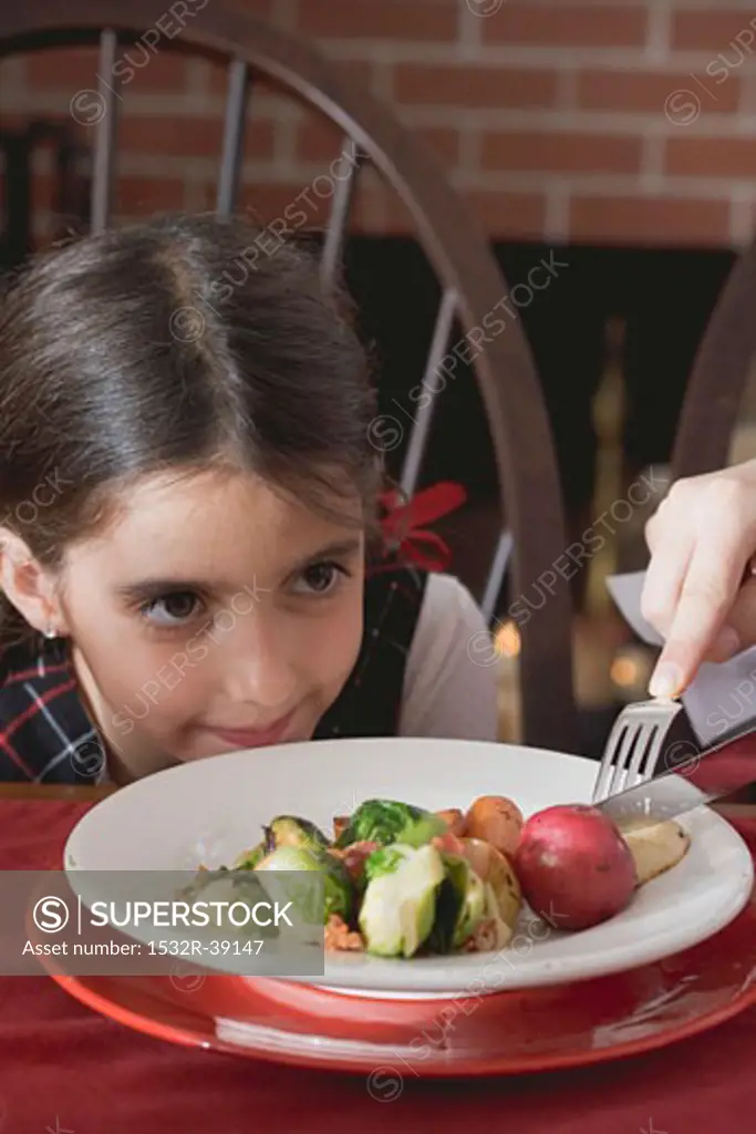 Hand cutting up vegetables on small girl's plate