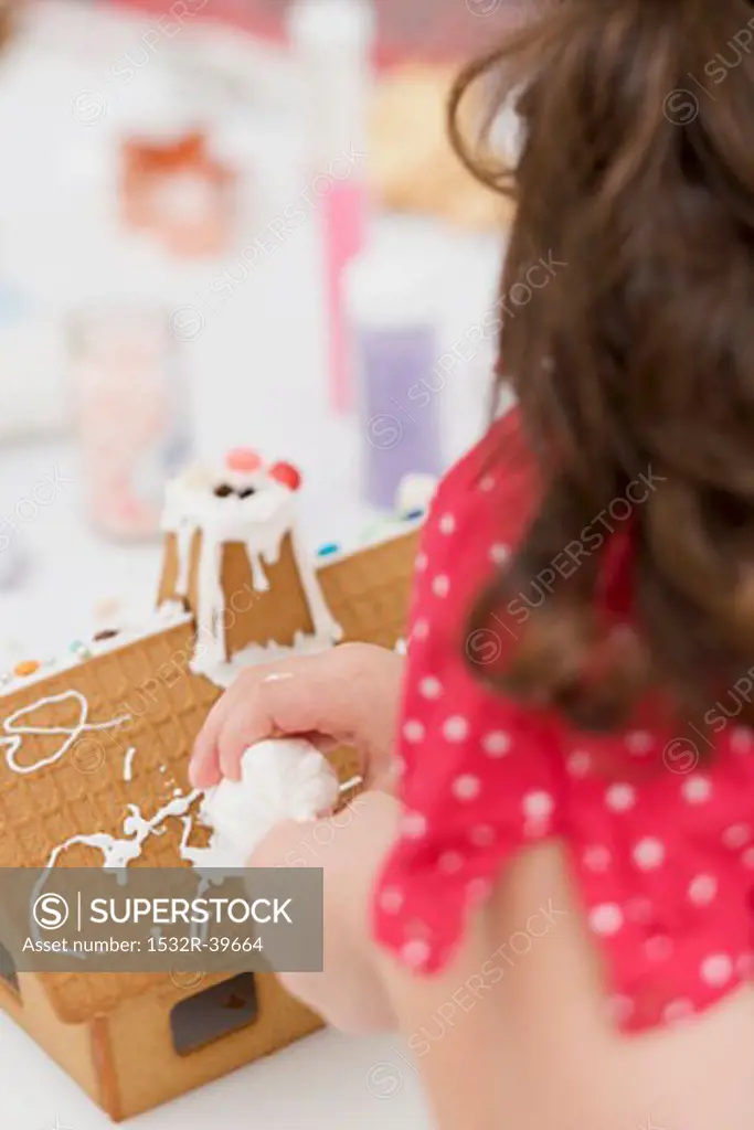 Small girl decorating gingerbread house using piping bag
