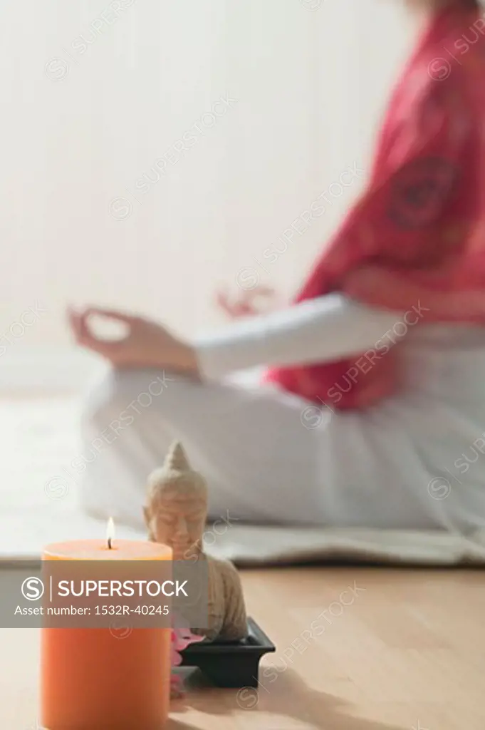 Woman sitting cross-legged, candle and Buddha statue