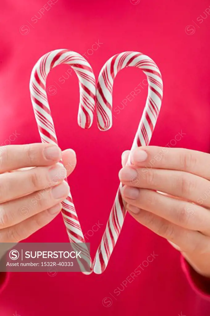 Woman holding two candy canes together to form a heart
