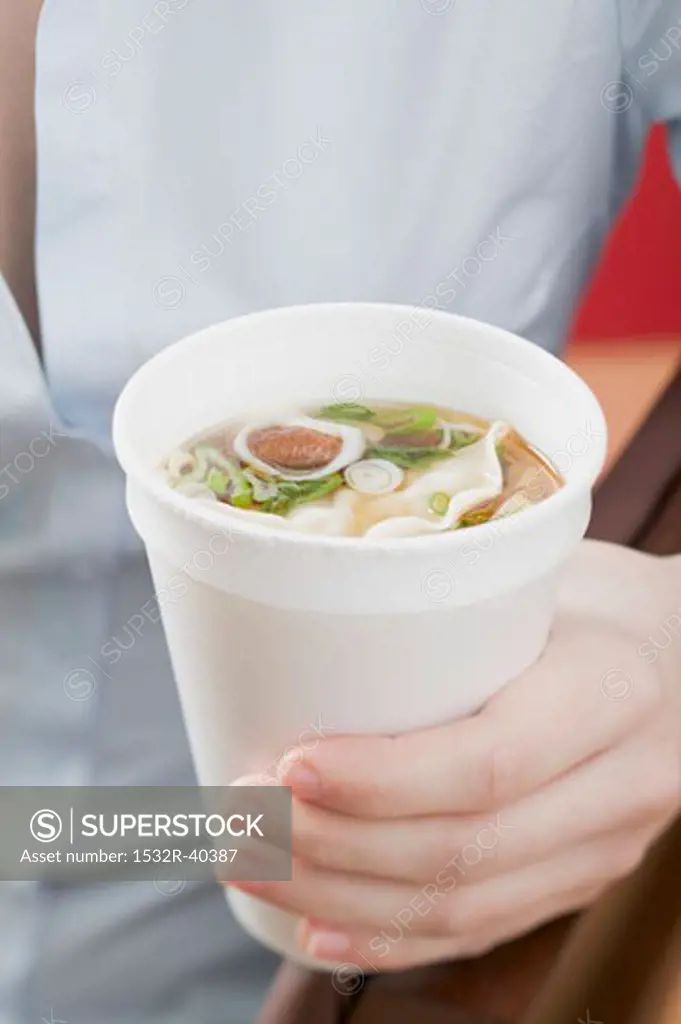 Woman holding paper cup of Asian noodle soup
