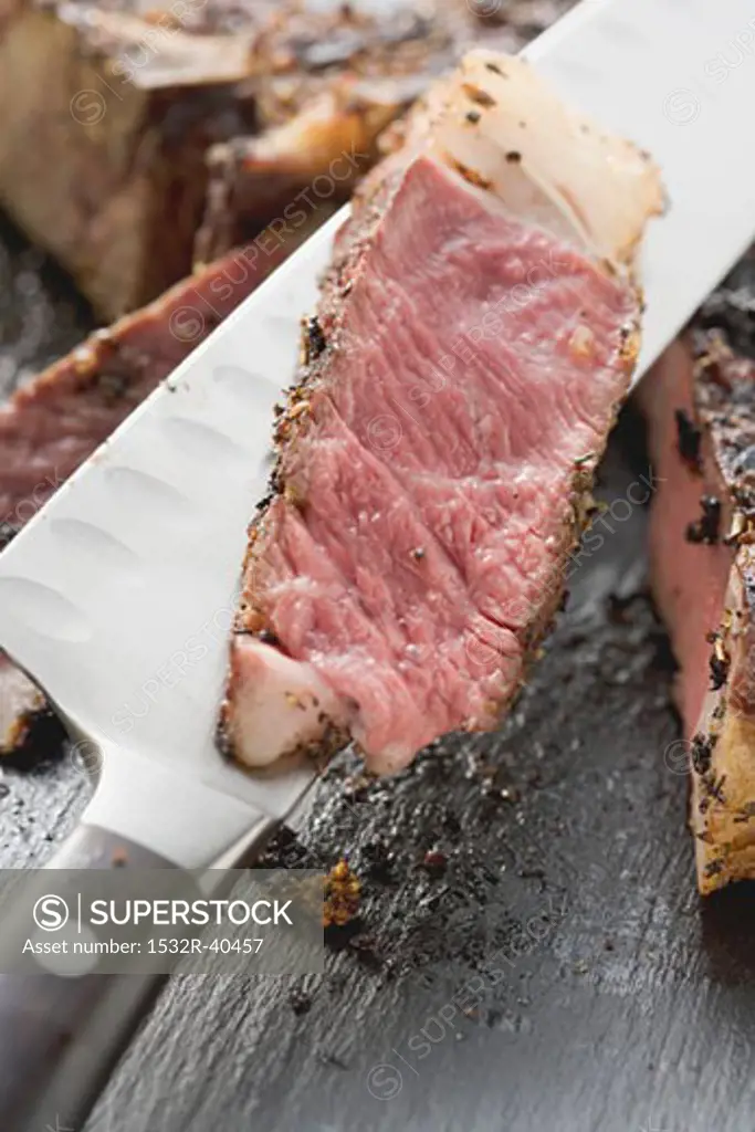 Slice of spicy rib eye steak on knife (close-up)