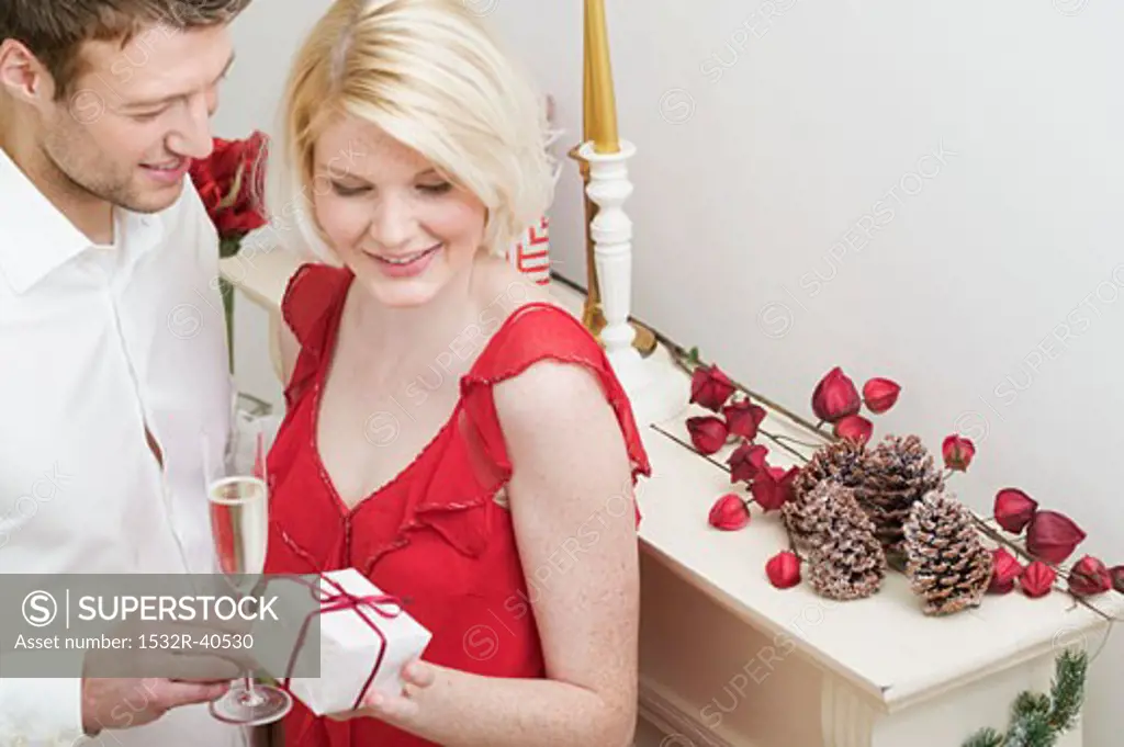 Man giving Christmas gift to woman by fireplace