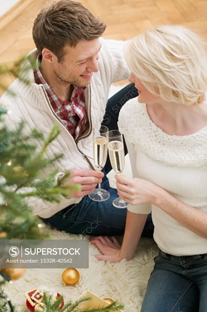 Couple clinking glasses of sparkling wine beside Xmas tree