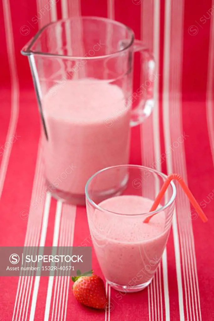 Strawberry milk in glass with straw, glass jug, strawberry