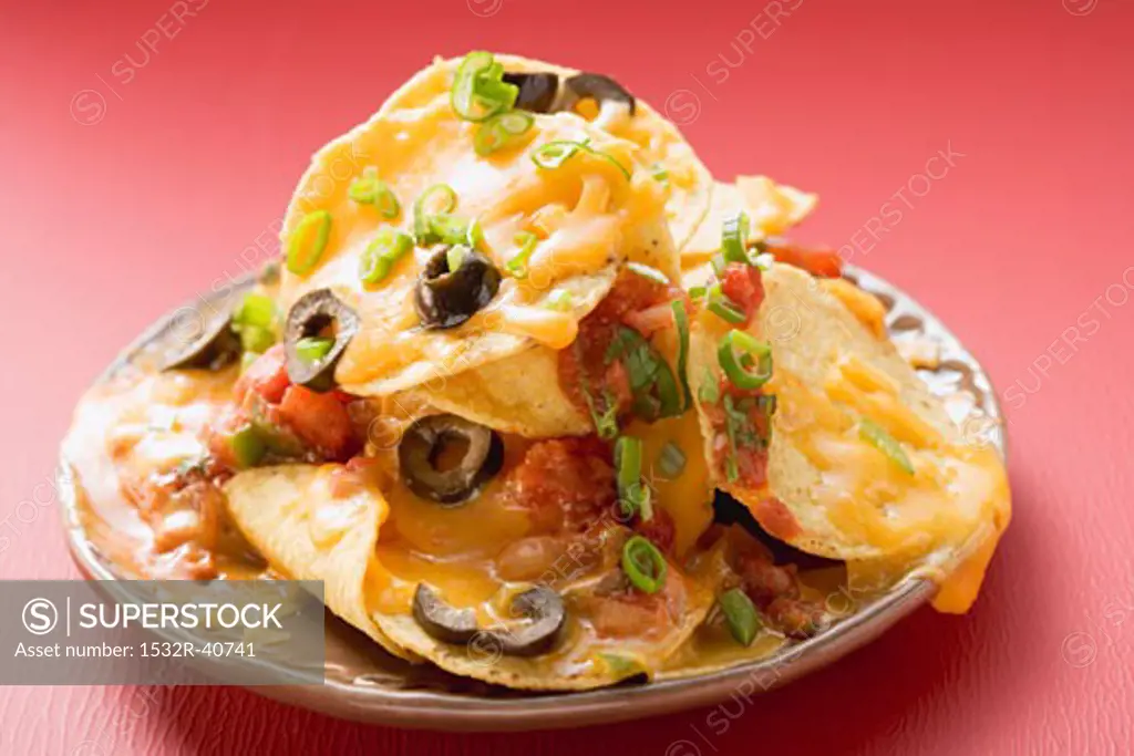 Tortilla chips with melted cheese and olives on plate