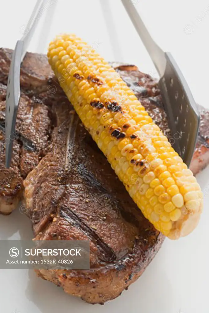 Grilled T-bone steak with corn on the cob and grill tongs