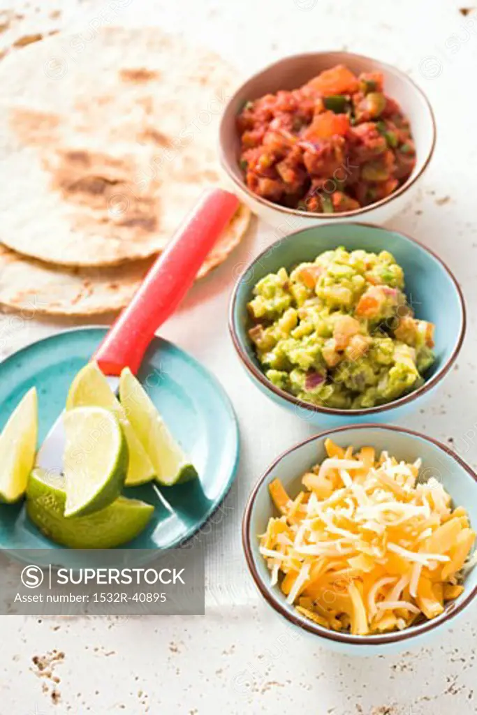 Tortillas, guacamole, salsa, grated cheese and lime wedges