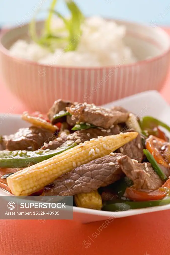 Beef with vegetables & sesame seeds, rice in background (Asia)