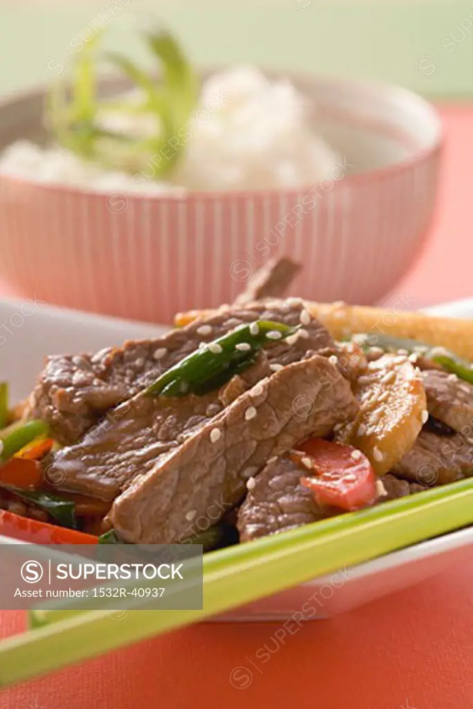 Beef with vegetables & sesame seeds, rice in background (Asia)