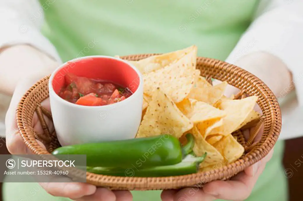 Hands holding basket of nachos with salsa and chilli