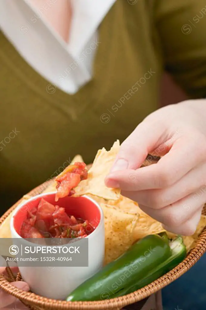 Woman dipping nacho in tomato salsa