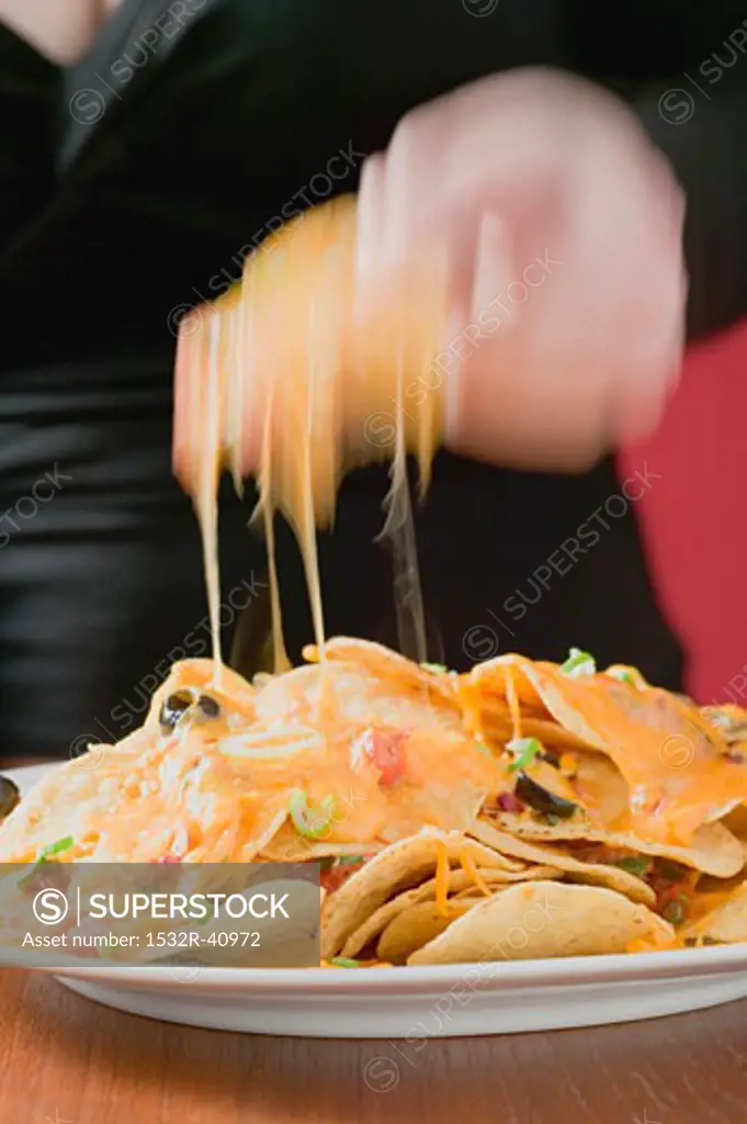 Hand taking tortilla chip with melted cheese from plate