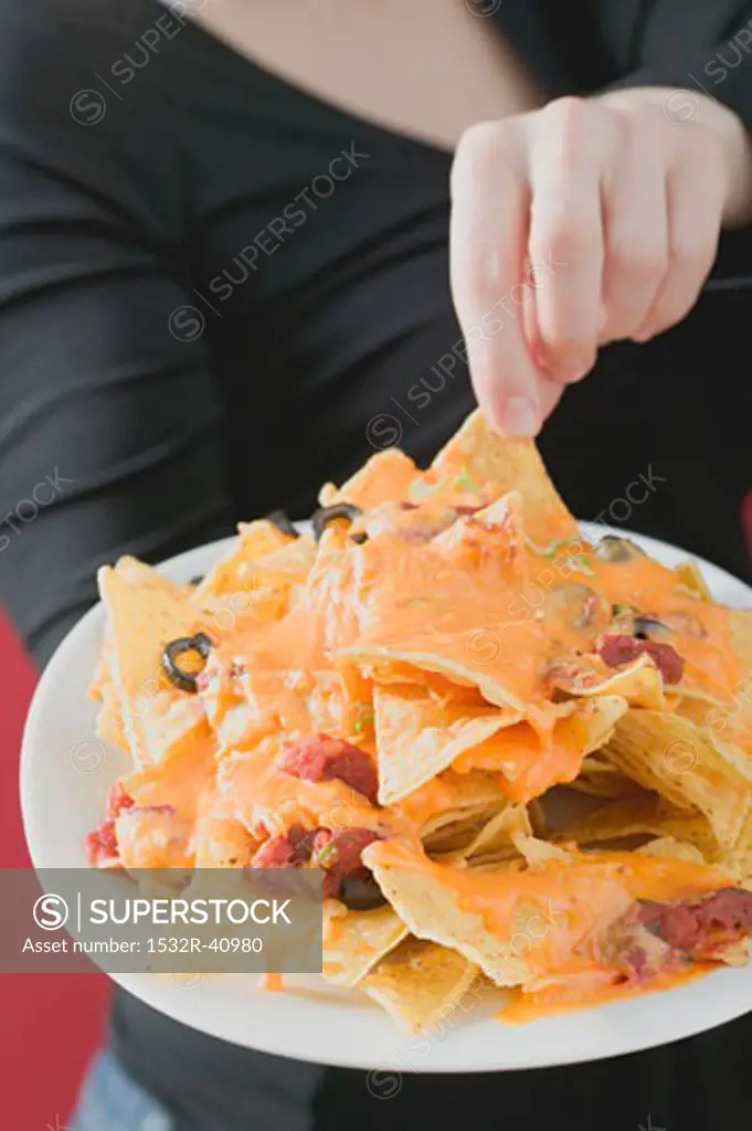 Woman reaching for nachos with melted cheese on plate