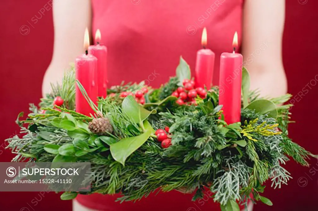 Woman holding Advent wreath with four burning candles