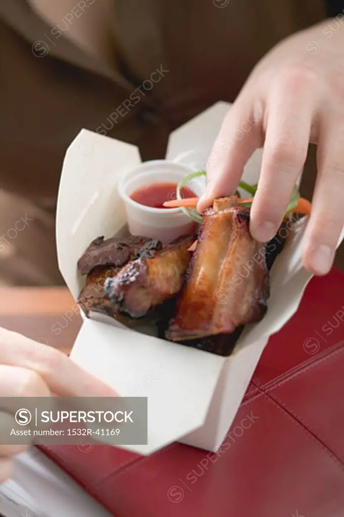 Woman taking glazed pork rib out of take-away container