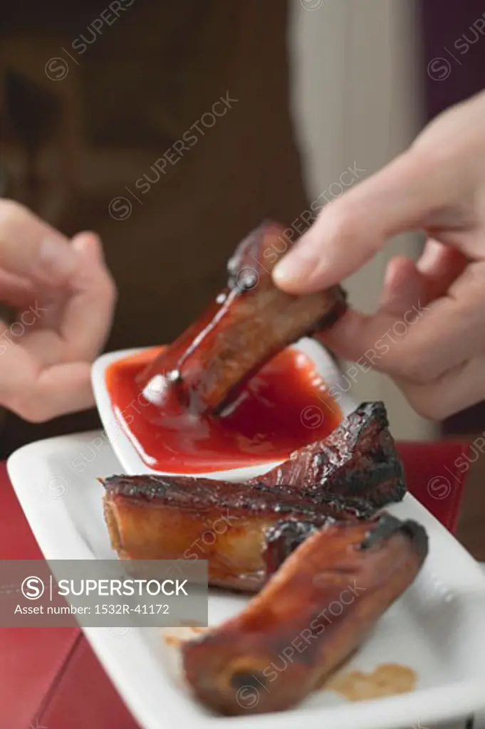 Woman dipping glazed pork rib in chilli sauce