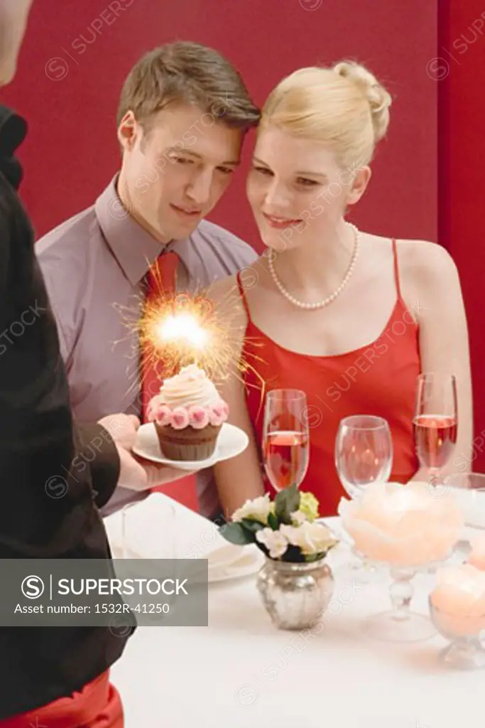 Waiter serving cupcake with sparkler to romantic couple